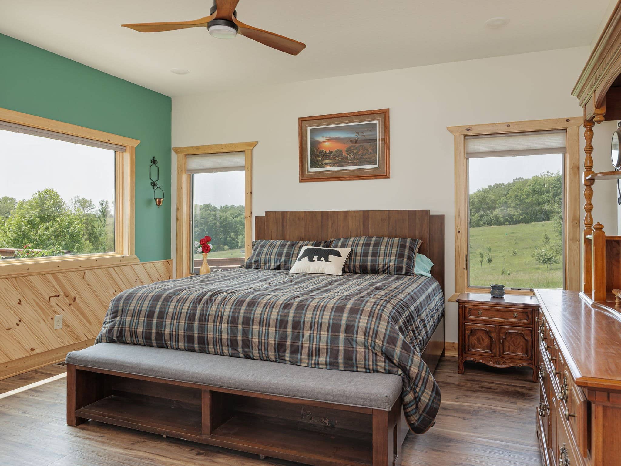 A guest bedroom at Selah Hills Ranch with plaid bedding, a green accent wall and windows on two sides.